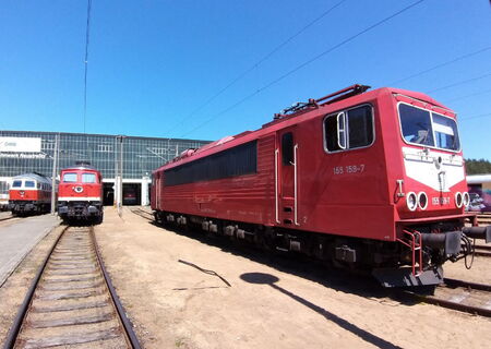Lokparade-Neustrelitz - rote Elektrolokomotive mit der Nummer 155 159-7 auf einem Gleis vor einem Bahndepot unter blauem Himmel.