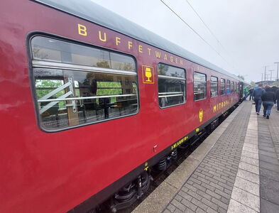 Sonderzug mit Außenansicht des Buffetwagens. Der Zug steht am Bahnsteig und Fahrgäste steigen ein.