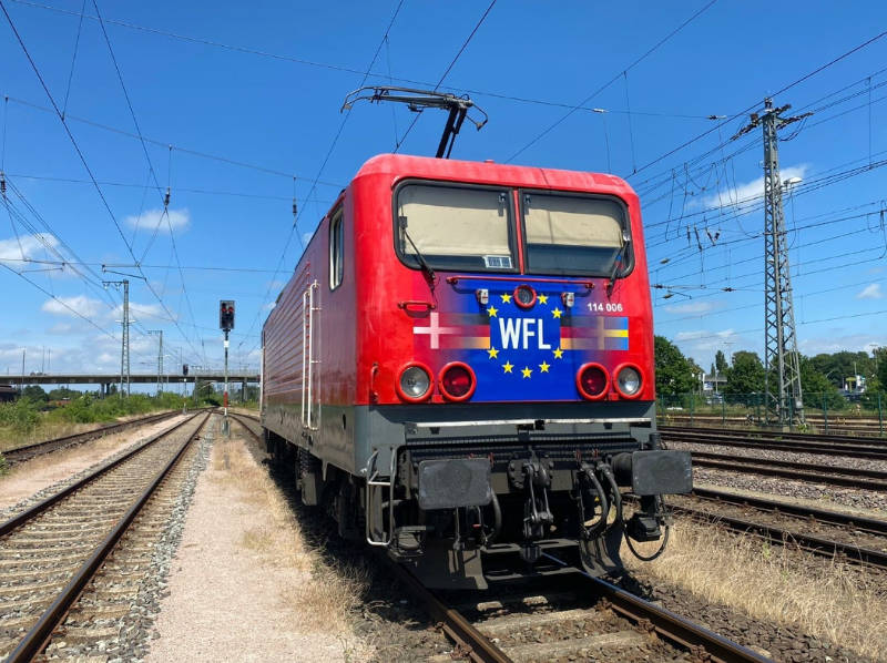 einzelne rote Elektrolokomotive Baureihe 114 auf ländlicher Strecke